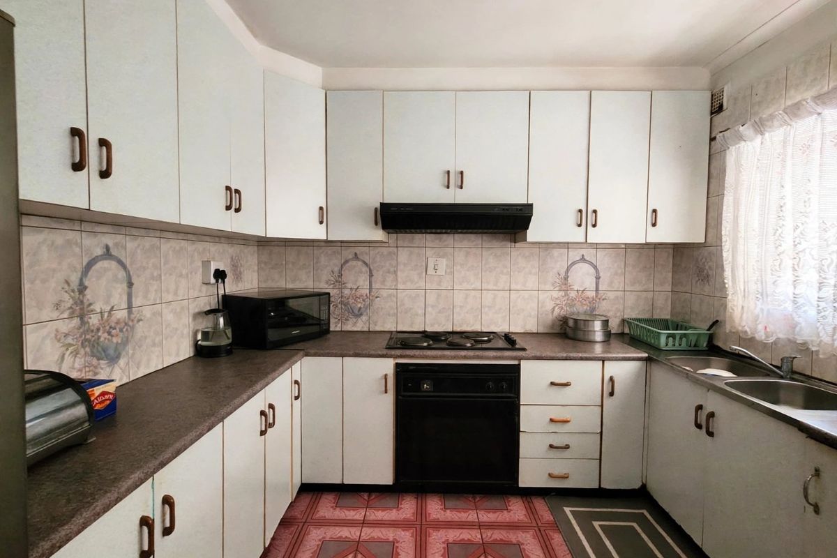 A functional kitchen featuring white cabinetry, laminate countertops, a built-in oven with hob, and a double bowl stainless steel sink.