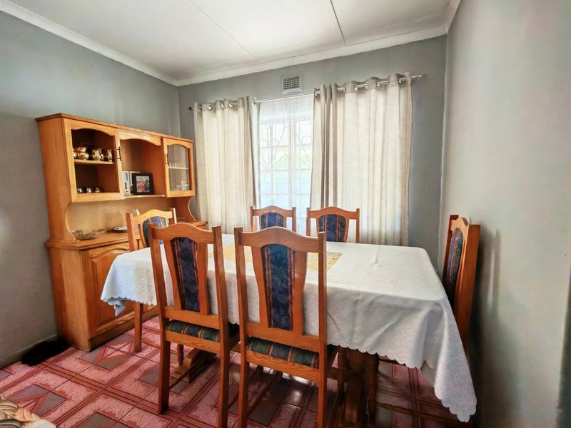 A functional dining room featuring tiled flooring, neutral wall tones, and a window fitted with security bars.