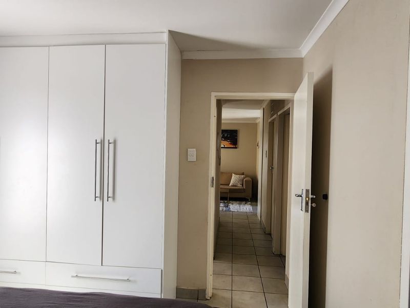 A bedroom featuring a large white built-in wardrobe with modern handles, neutral wall tones, and access to a tiled hallway.
