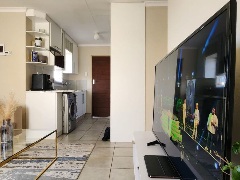 Open-plan living area featuring tiled flooring and a compact kitchen with built-in cabinetry and laundry plumbing connections.