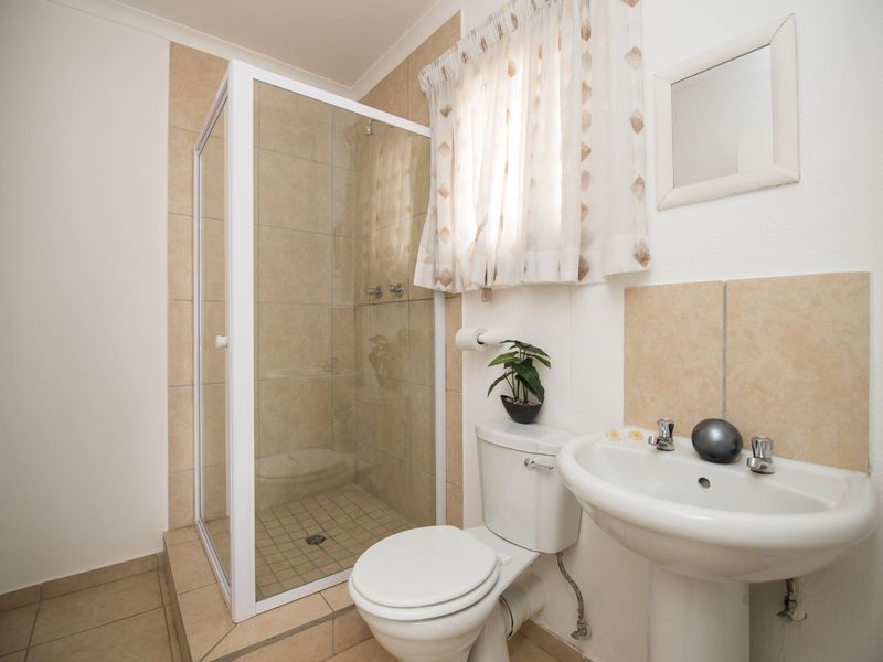 A functional bathroom featuring a glass-enclosed shower, pedestal basin, and toilet with neutral tiled finishes.