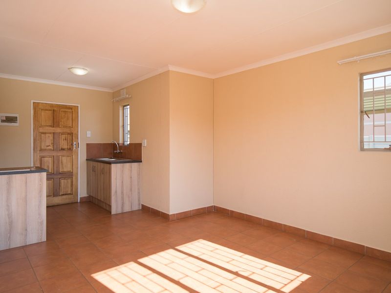 An open-plan living area featuring tiled flooring, a compact kitchenette with sink, and secure window bars, offering a clean and functional blank canvas.