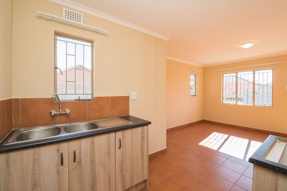 An empty kitchen area featuring tiled flooring, laminate cabinetry, a double bowl stainless steel sink, and security bars on the windows.