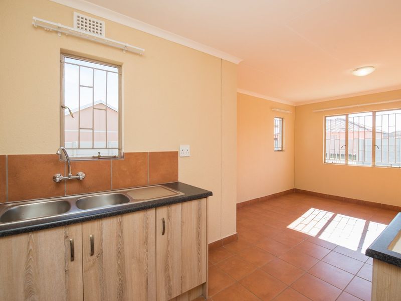 An empty kitchen area featuring tiled flooring, laminate cabinetry, a double bowl stainless steel sink, and security bars on the windows.