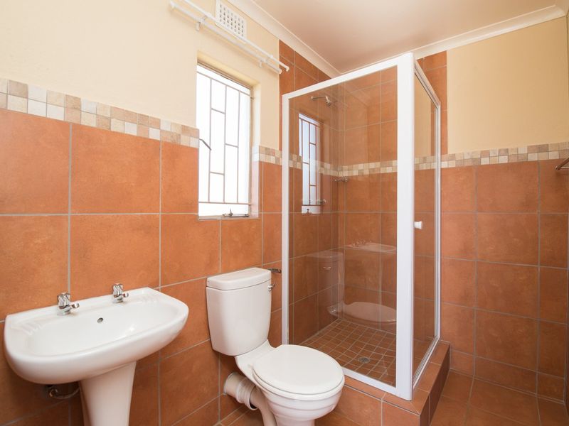 A functional bathroom featuring a pedestal basin, toilet, and a glass-enclosed shower with terracotta-toned wall and floor tiling.