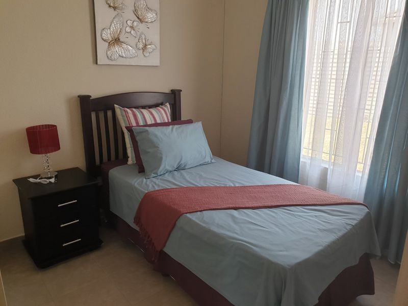 A well-maintained bedroom featuring tiled flooring and a window fitted with security bars, providing a clean and functional living space.