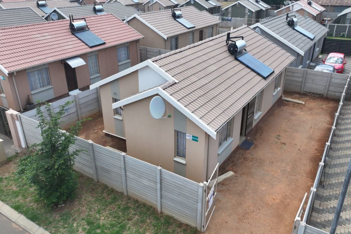 Aerial view of a residential property featuring a tiled roof with a solar water heater, enclosed by precast concrete walling and a metal gate.
