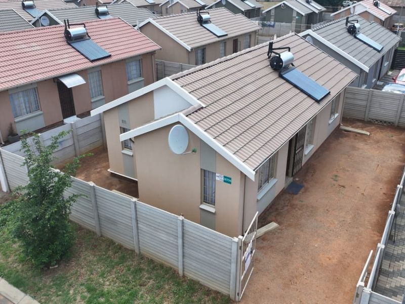 Aerial view of a residential property featuring a tiled roof with a solar water heater, enclosed by precast concrete walling and a metal gate.
