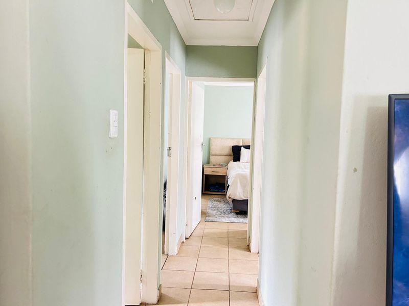 A functional hallway with tiled flooring and neutral wall paint, providing access to adjacent rooms including a bedroom.