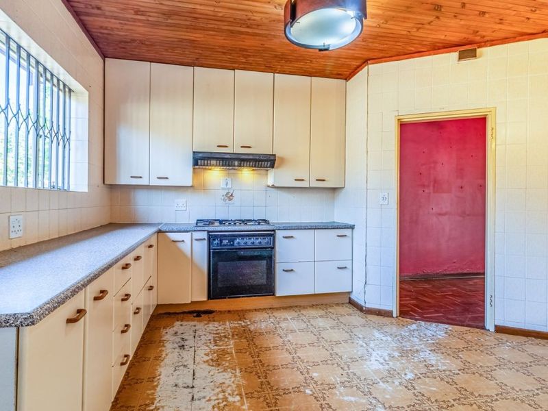 A dated kitchen featuring built-in cabinetry, a gas hob with extractor, and tiled walls, requiring floor restoration and cosmetic updates to modernize the space.