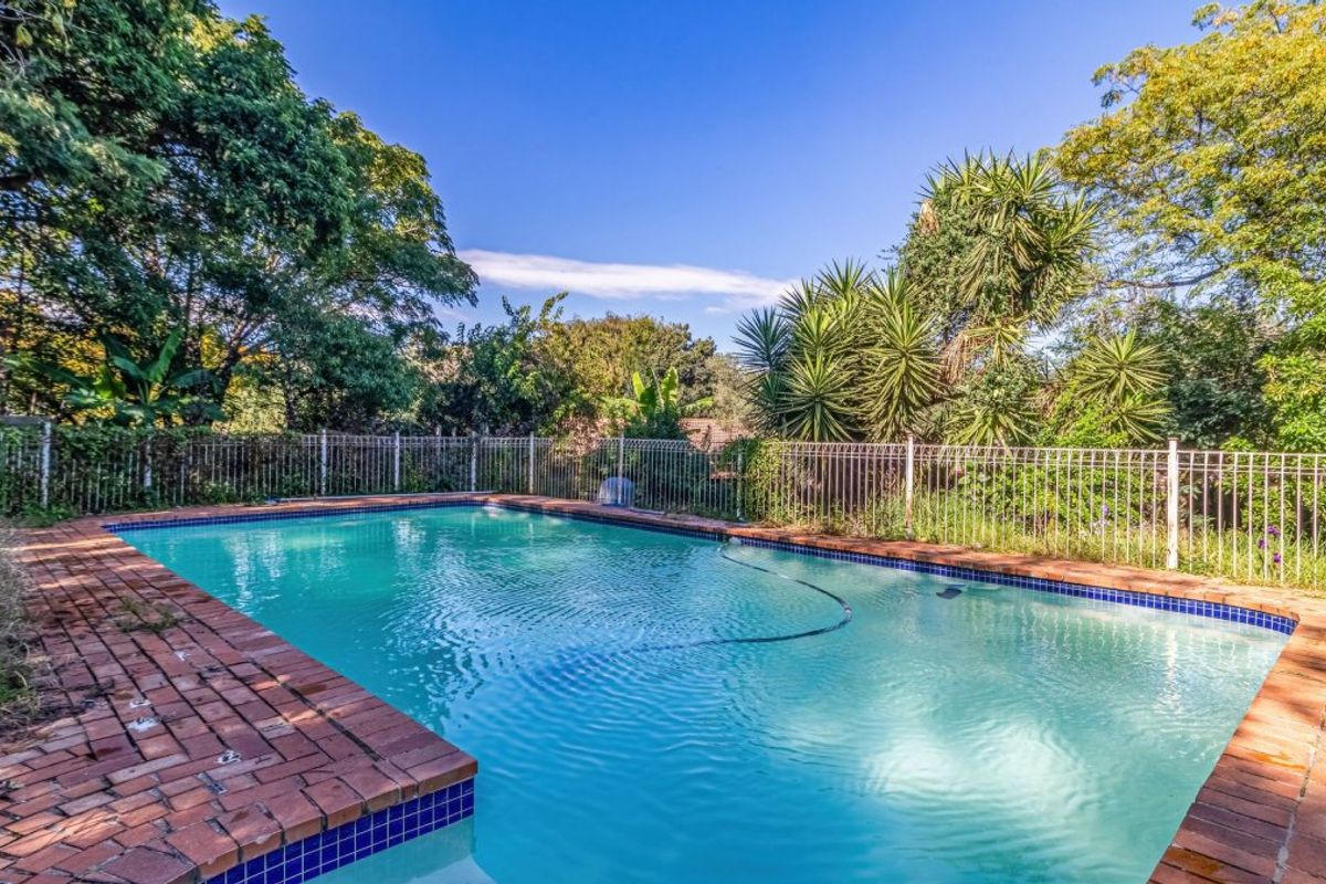 A private swimming pool area featuring brick coping and secure metal perimeter fencing, surrounded by established garden greenery.