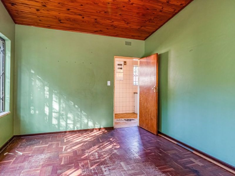 An empty bedroom featuring parquet flooring, a timber ceiling, and a security gate on the window, leading to an adjacent tiled utility area.
