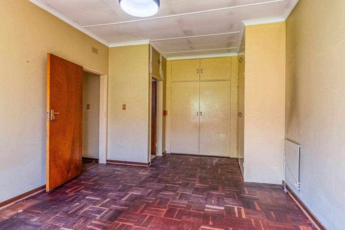 An empty bedroom featuring original parquet flooring, built-in cupboards, and neutral wall finishes, offering a blank canvas for renovation.