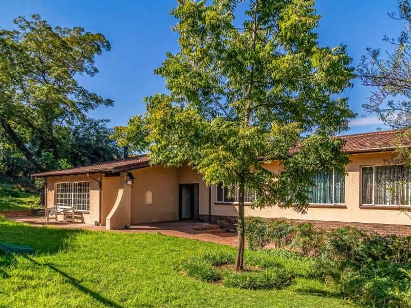 Rear view of the house featuring a paved patio area, brick and plaster exterior, and large windows overlooking a spacious garden.