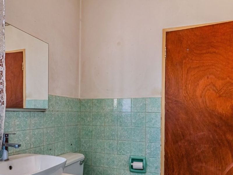 A dated bathroom featuring light blue ceramic wall tiles, a basic basin, and a wooden door. The space is ready for a modern renovation.