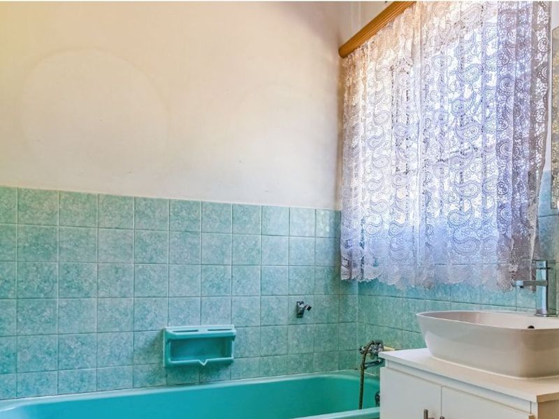 A dated bathroom featuring a turquoise bathtub, matching tiled splashback, and a modern vessel sink on a vanity cabinet.