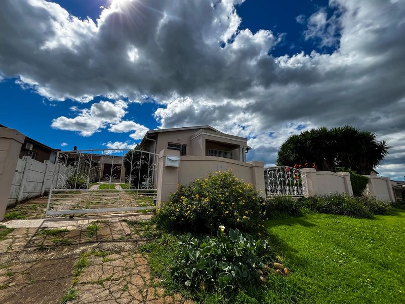 Front view of the property featuring a gated entrance, perimeter wall, and paved driveway set against a landscaped garden.