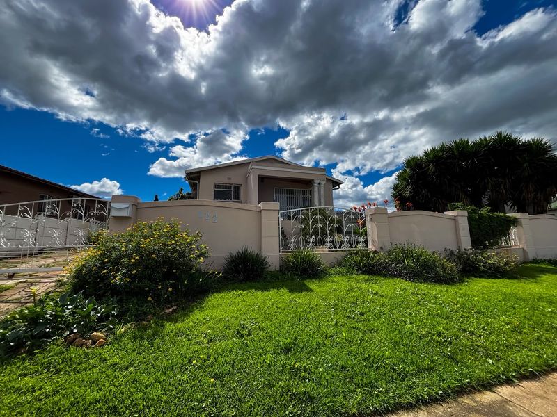 Front view of a residential property featuring a well-maintained garden, perimeter wall with wrought iron fencing, and a secure gated entrance.