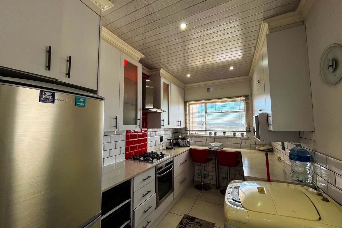 A functional kitchen featuring white cabinetry, stone countertops, a gas hob with extractor fan, and a distinctive tongue and groove ceiling with recessed lighting.