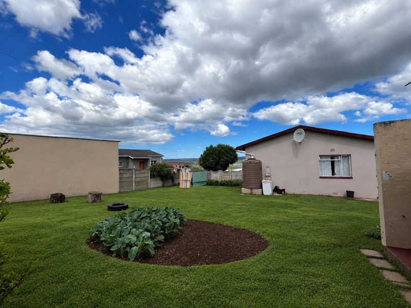 A spacious rear garden featuring a lawn, a circular vegetable patch, a water storage tank, and a precast concrete boundary wall.