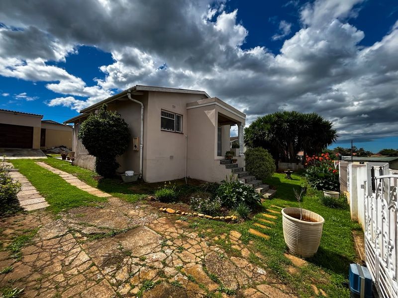 Front view of a residential property featuring a stone paved driveway, concrete entrance steps, and established garden area with boundary wall and gate.