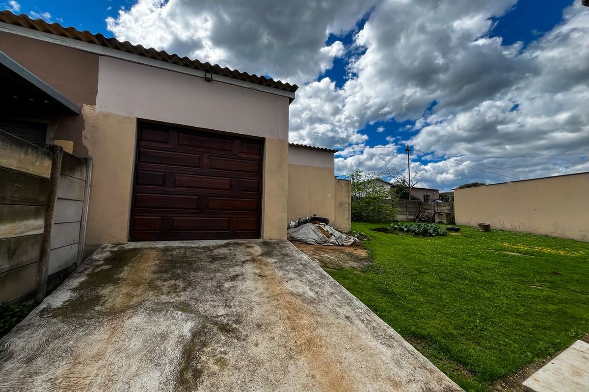Rear view of the property featuring a garage with a wooden door, a concrete driveway, and a spacious grass garden area.