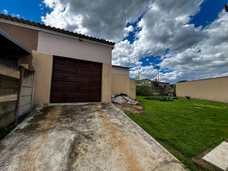 Rear view of the property featuring a garage with a wooden door, a concrete driveway, and a spacious grass garden area.