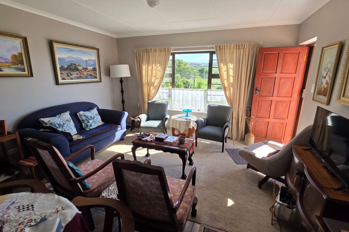 A comfortable living room featuring carpeted flooring, a solid timber panel door, and large windows providing natural light and garden views.