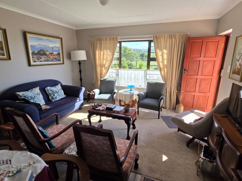 A comfortable living room featuring carpeted flooring, a solid timber panel door, and large windows providing natural light and garden views.
