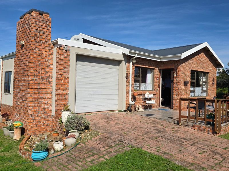 A single-story face-brick house featuring a front-facing garage, a paved driveway, and an attached timber deck entrance.