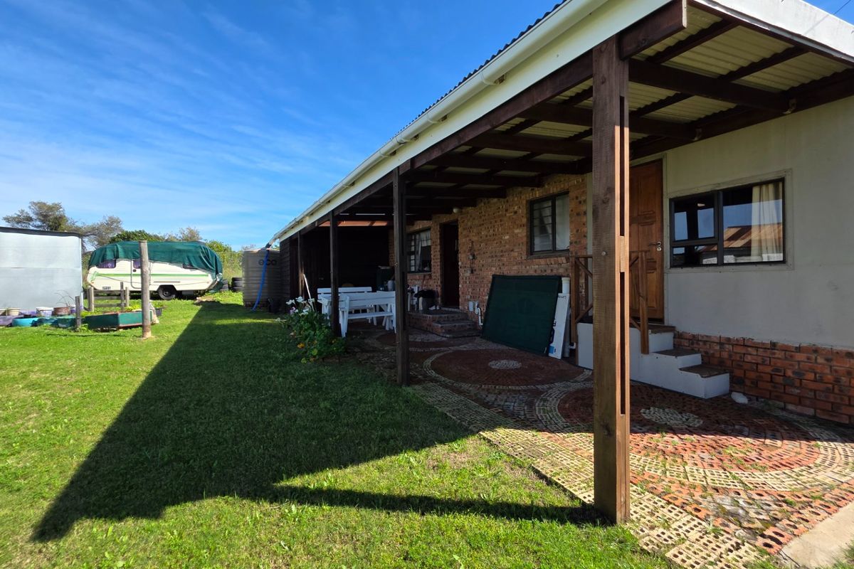 Rear view of the property featuring a covered patio area with brick paving and timber support posts, overlooking a spacious garden.