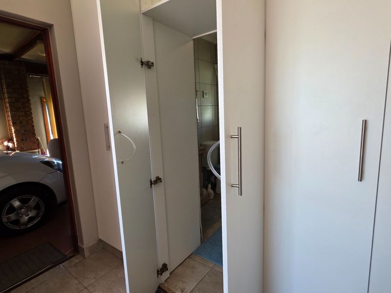 A functional hallway featuring built-in storage cupboards with modern handles and tiled flooring, providing access to adjacent rooms.
