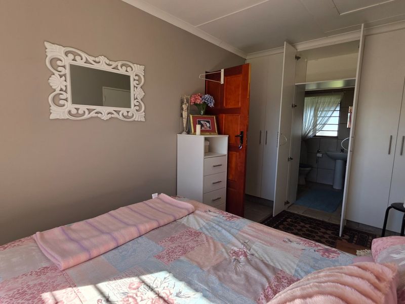 A bedroom featuring built-in cupboards and an adjoining en-suite bathroom with a pedestal basin and toilet.