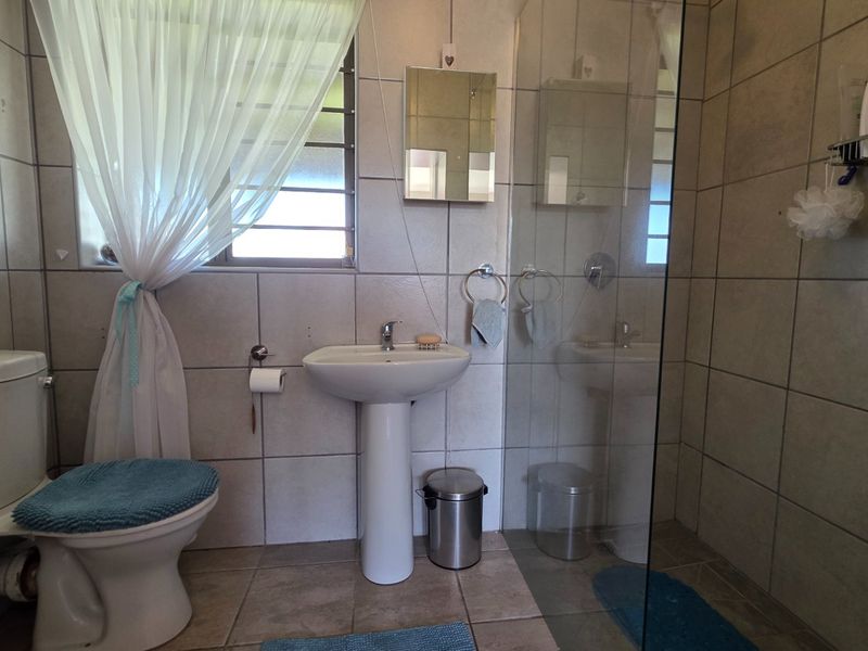 A functional bathroom featuring a pedestal basin, toilet, and a glass-enclosed shower with neutral wall and floor tiling.