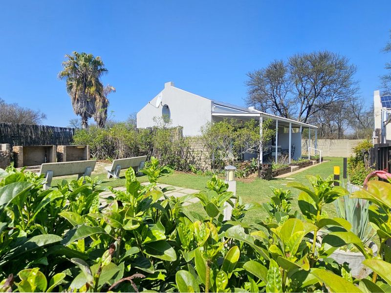 Rear exterior view featuring a covered patio, built-in braai area, landscaped garden, and solar panels installed on the roof.