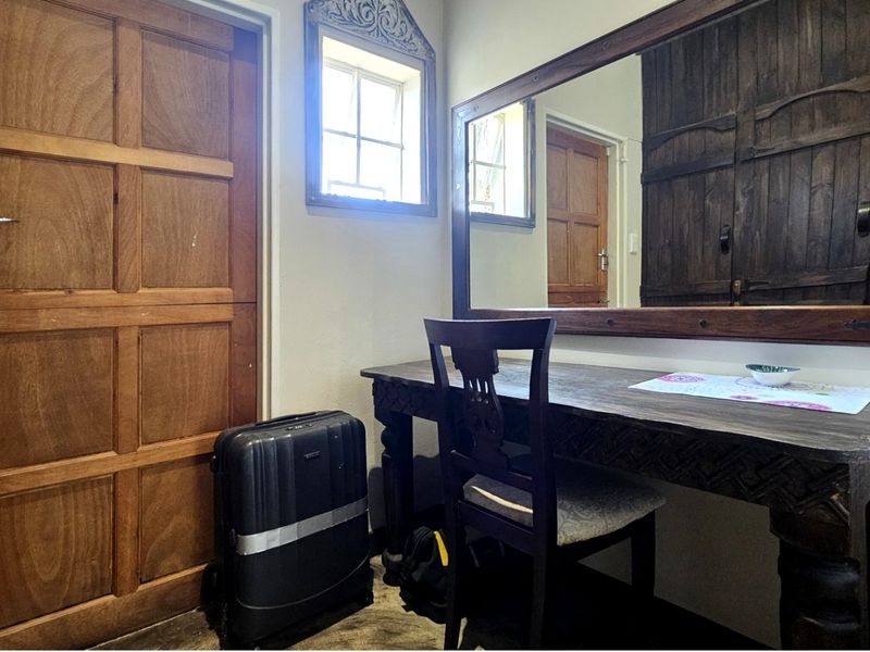 A bedroom interior featuring a wooden door, a large wall-mounted mirror, and a small window, providing a functional space with traditional wooden elements.