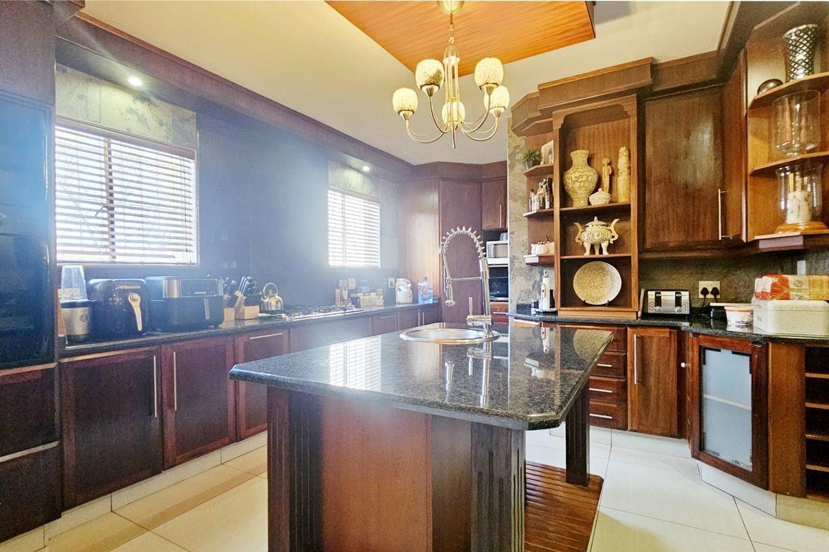 Spacious kitchen featuring dark wood cabinetry, granite countertops, a central island with a sink, and tiled flooring, offering a classic and functional workspace.