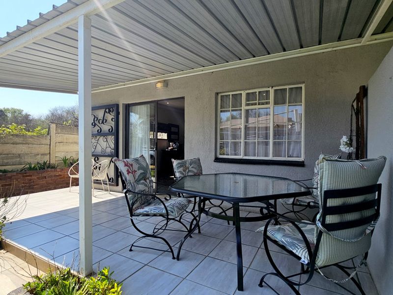 A covered outdoor patio featuring tiled flooring, a corrugated metal roof, and direct access to the interior through a sliding glass door.