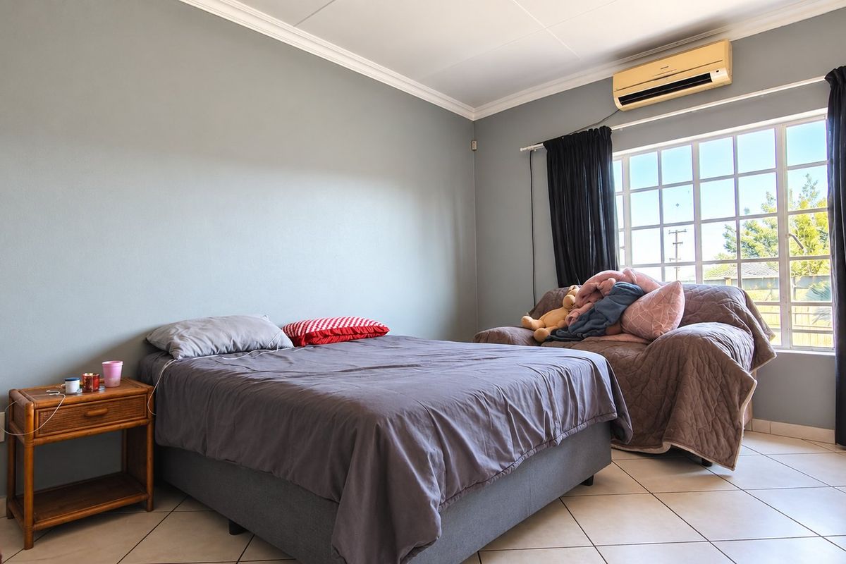 A bedroom featuring tiled flooring, cornicing, and a wall-mounted air conditioning unit, providing a functional space with natural light from the grid-pattern window.