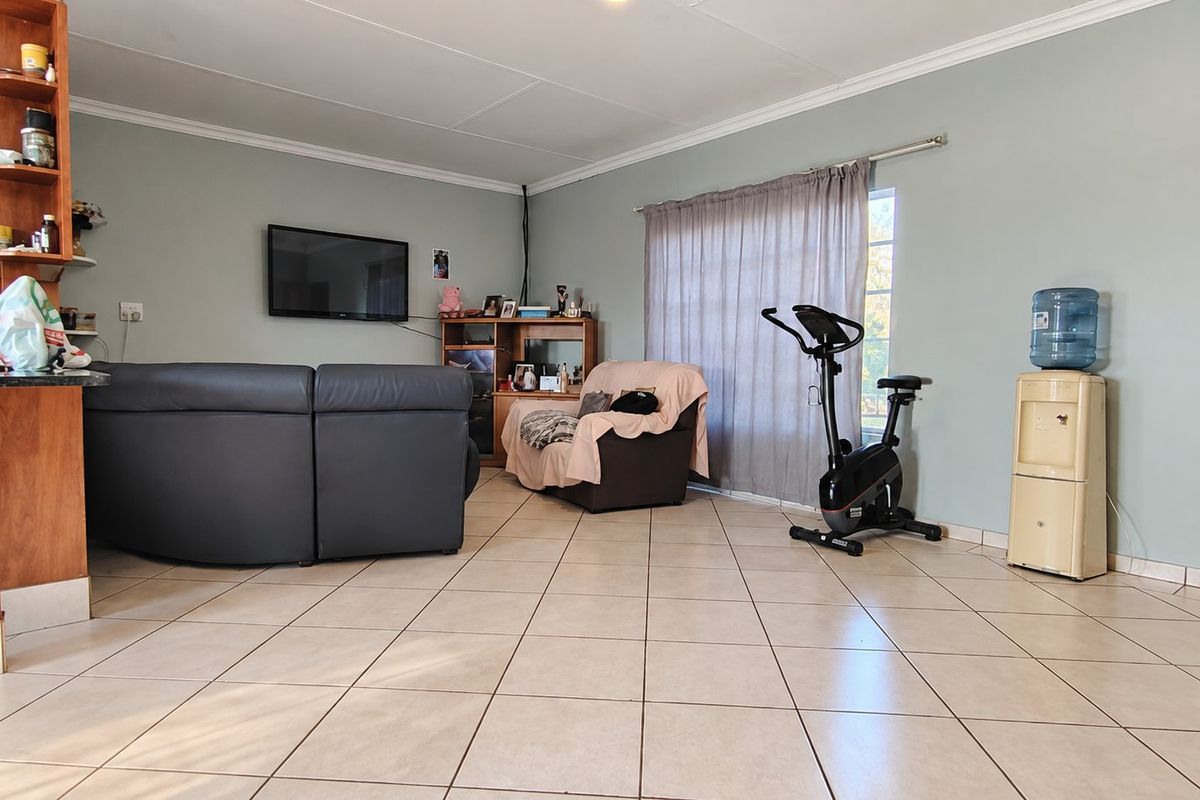 A spacious living area featuring neutral tiled flooring, coved ceilings, and a large window with curtain rails, offering a functional and open layout.