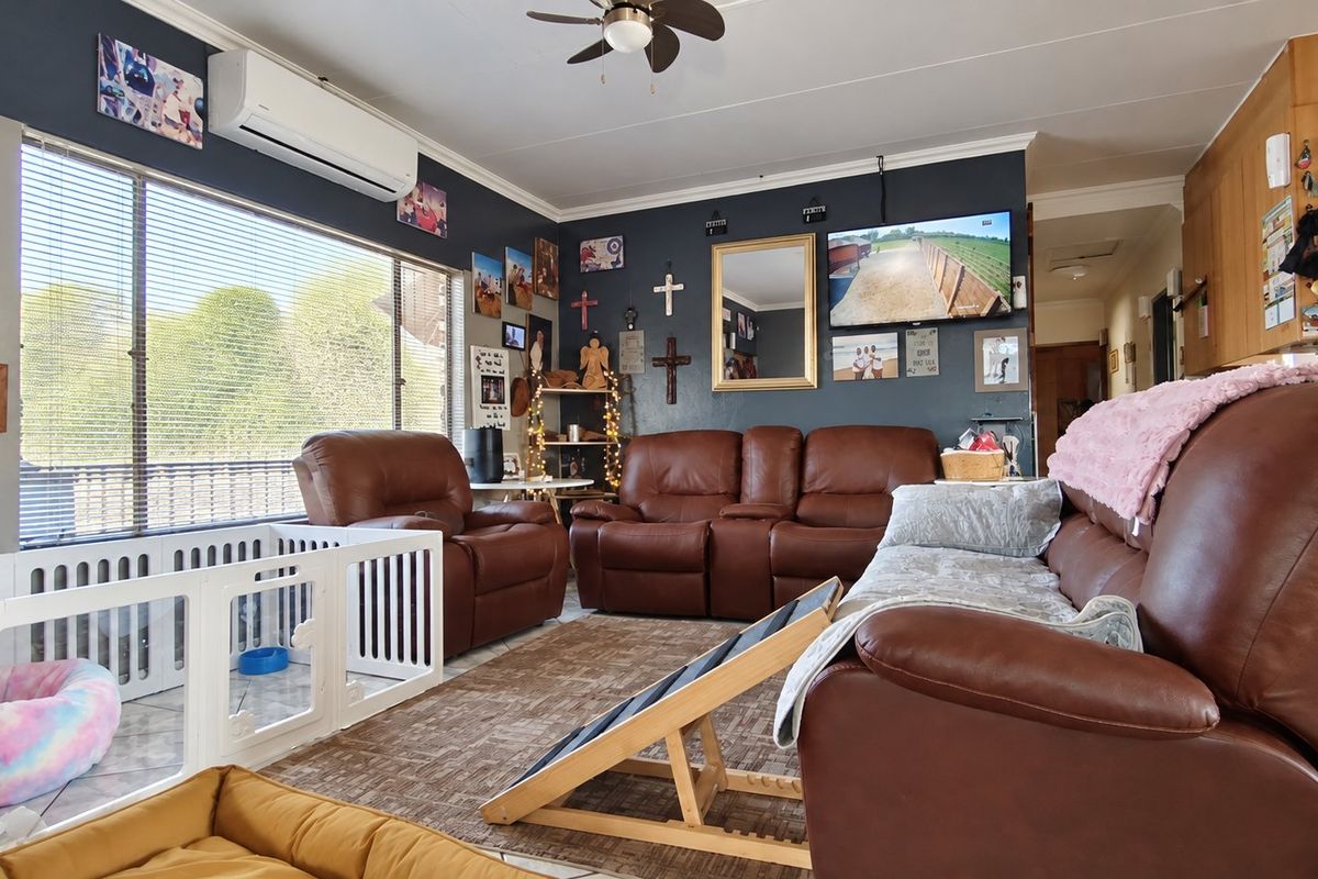 A comfortable living room featuring tiled flooring, a ceiling fan, and a wall-mounted air conditioning unit, providing a functional and relaxed living space.