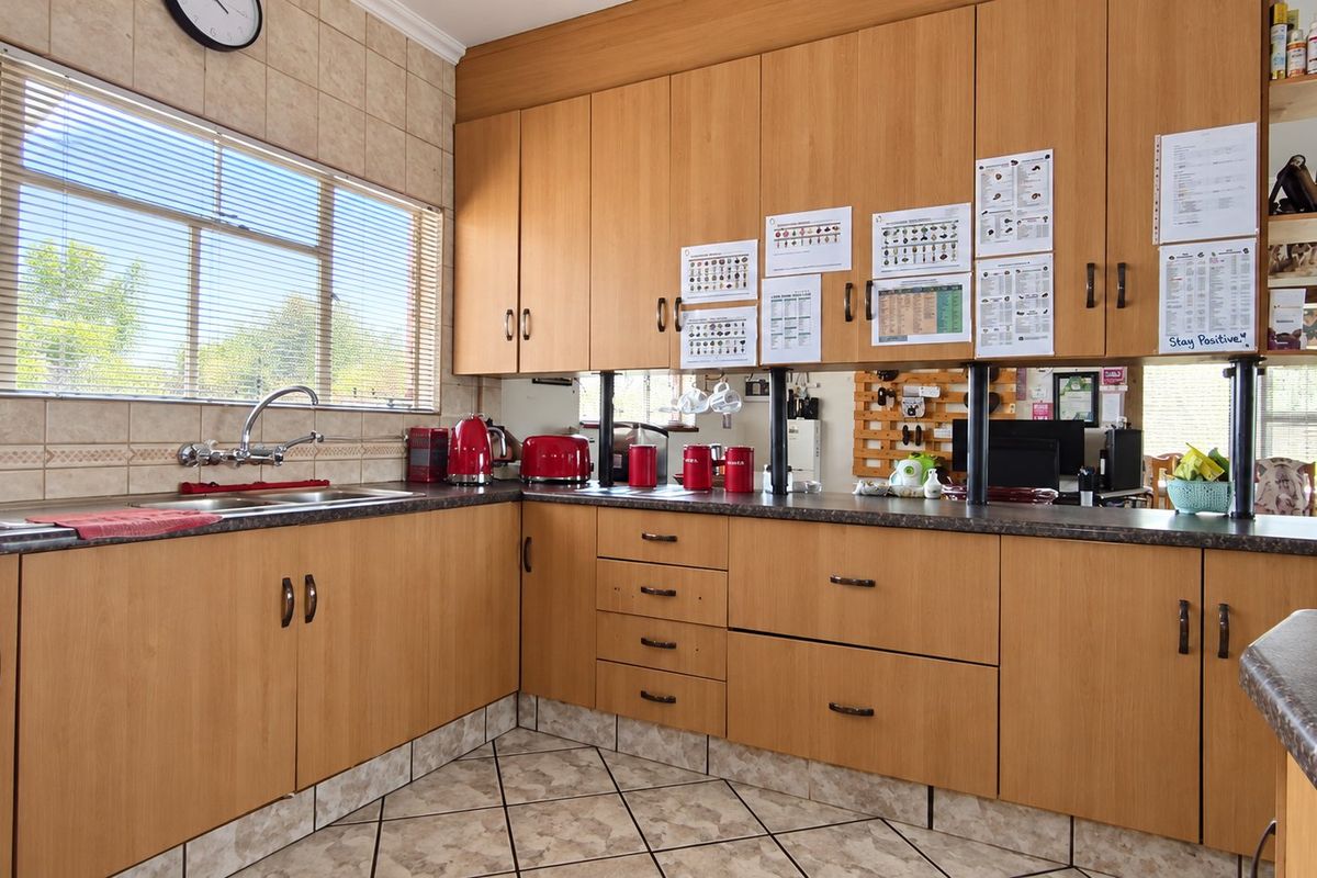 A functional kitchen featuring light wood-look laminate cabinetry, dark laminate countertops, a double basin sink, and tiled finishes throughout.