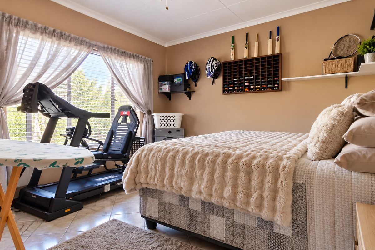 A well-maintained bedroom featuring tiled flooring, neutral wall tones, and functional window treatments, currently utilized as a multi-purpose living and exercise space.