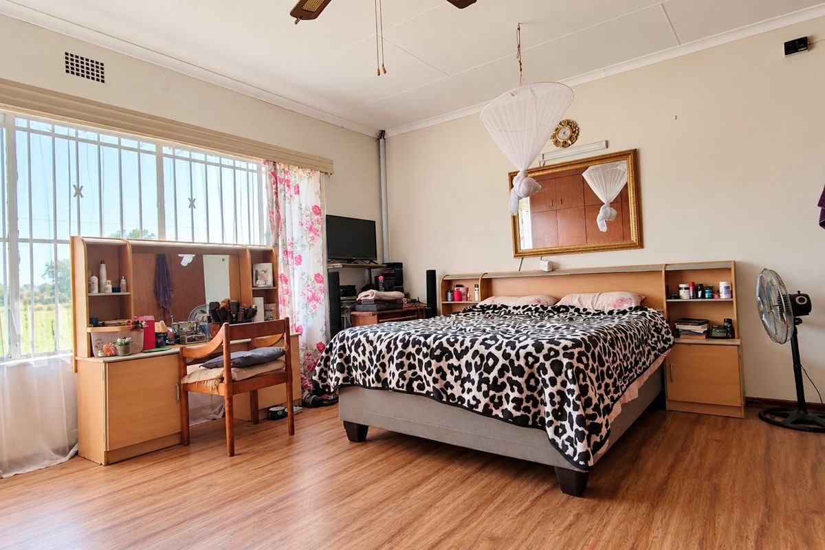 Spacious bedroom featuring laminate flooring, built-in cupboards, and large windows with security bars, offering a functional and well-lit living space.