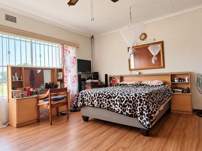 Spacious bedroom featuring laminate flooring, built-in cupboards, and large windows with security bars, offering a functional and well-lit living space.