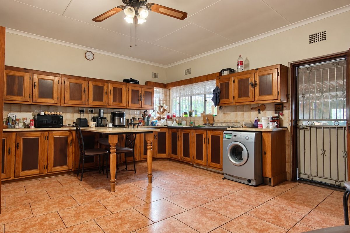 Spacious kitchen featuring traditional wooden cabinetry, tiled flooring, and a built-in washing machine, offering a functional layout with ample storage space.
