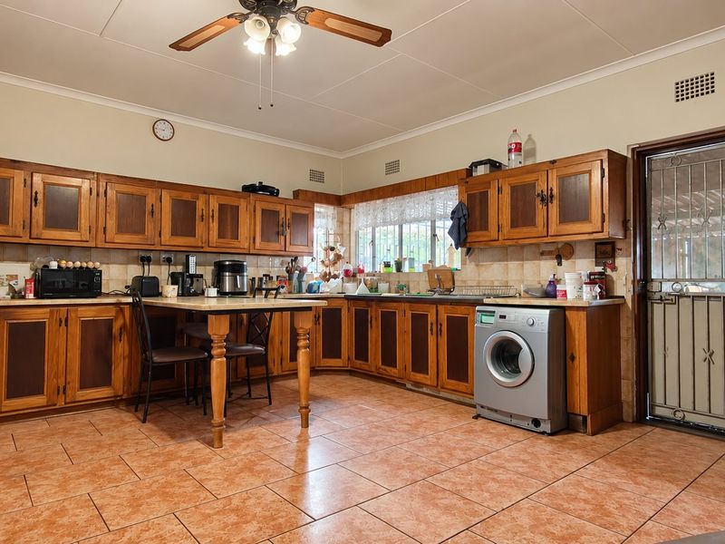 Spacious kitchen featuring traditional wooden cabinetry, tiled flooring, and a built-in washing machine, offering a functional layout with ample storage space.