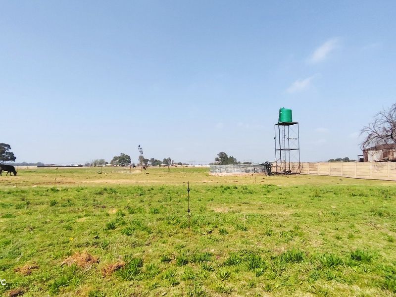 Expansive farm land featuring a raised water tank on a steel stand and perimeter boundary walling.
