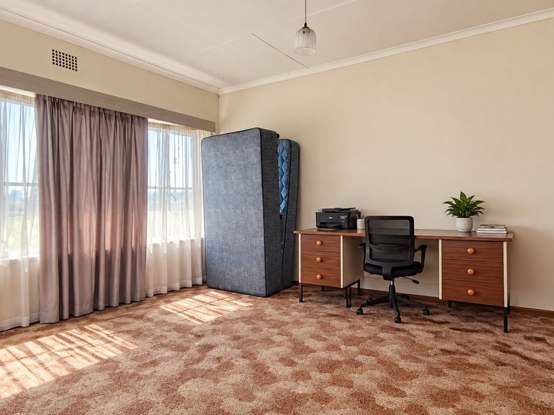 A bedroom featuring built-in wooden wardrobes, large windows allowing natural light, and patterned carpet flooring.