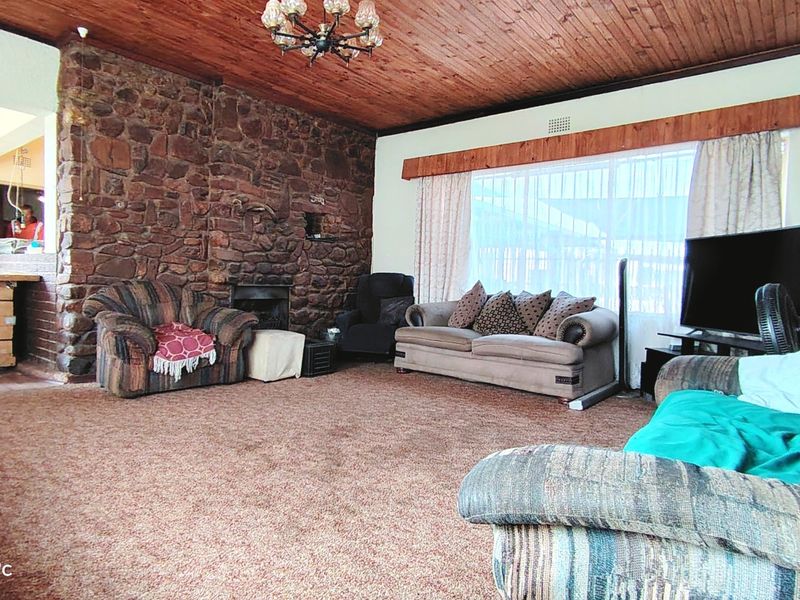 Spacious living room featuring a rustic stone fireplace, warm timber ceiling, and large windows, offering a cozy atmosphere with potential for modern updates.